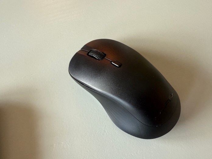 A close-up view of the JLab Flow wireless mouse showing its ergonomic design, scroll wheel, and side buttons against a light-colored surface.