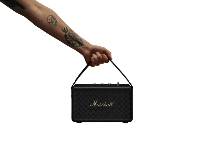 A hand holding the Marshall Kilburn III portable Bluetooth speaker, showcasing its vintage design and built-in strap.