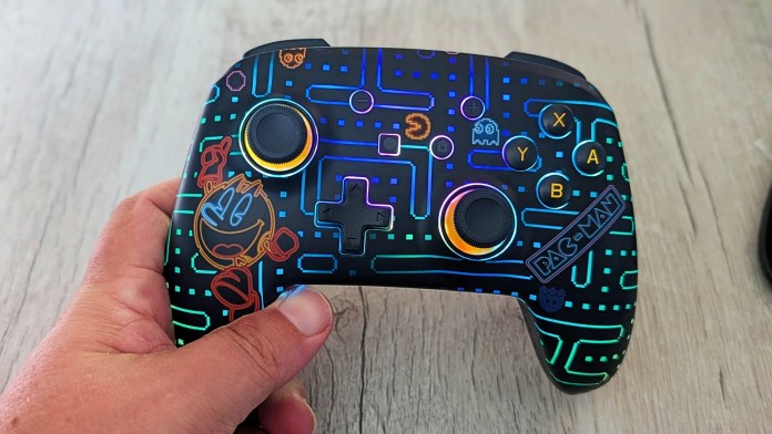 A hand holds a PowerA Pac-Man Neon Arcade Controller, featuring vibrant RGB lighting and a design inspired by the classic Pac-Man arcade game.