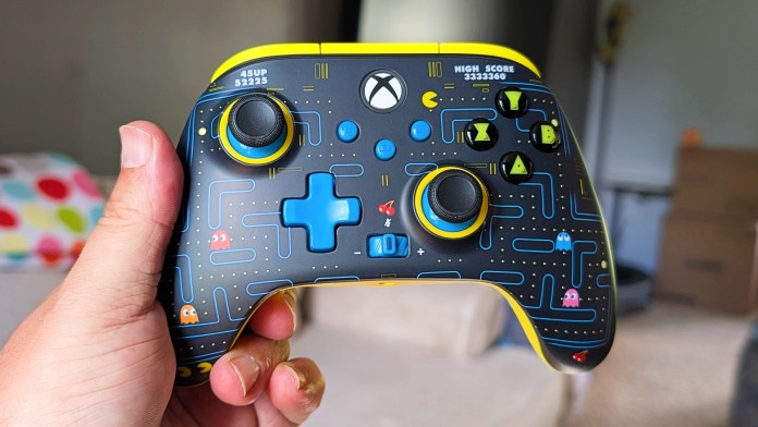 A close-up of a PowerA Pac-Man Wireless Controller for Xbox, featuring a colorful design with iconic Pac-Man imagery and retro arcade elements, held in a person's hand.