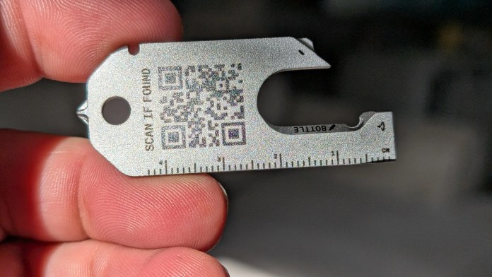 A person holding a small multi-tool with QR code and measurement markings, designed for convenience and functionality.