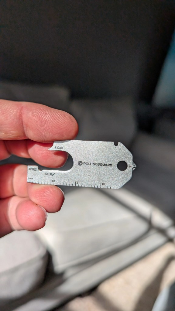 A person holding a compact and sleek multi-tool from Rolling Square, featuring various functions like a ruler and a bottle opener.