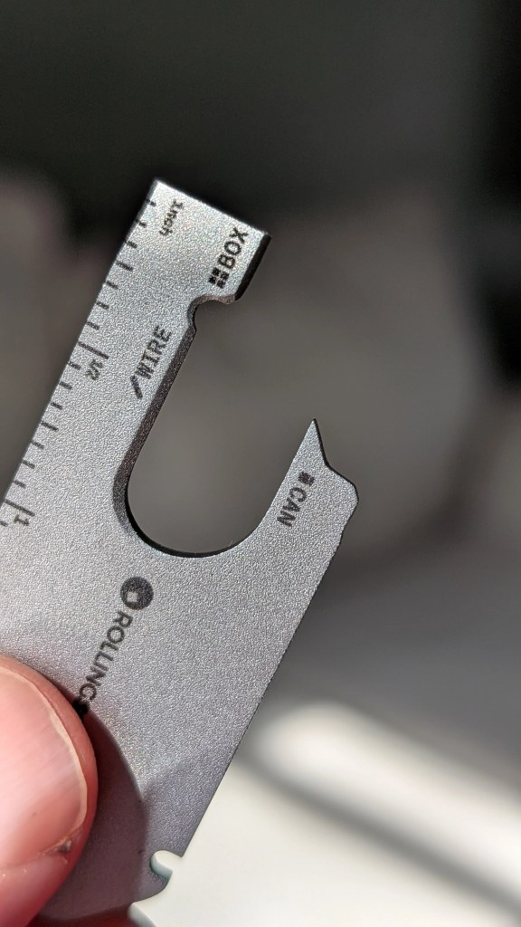 Close-up of Rolling Square AirNotch Pro Multi-tool with measuring scale and various tool functions, held in a hand.