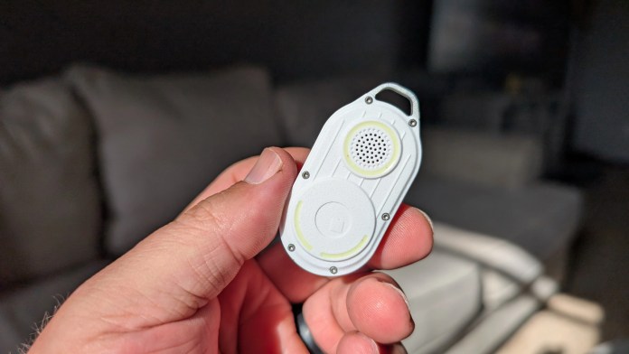 A person holding the Rolling Square AirCard Pro, a compact Bluetooth tracker, showcasing its sleek design with speaker holes and LED indicators against a blurred background.