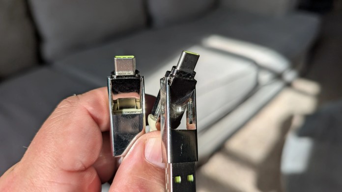 Close-up of a hand holding two USB-C connectors, showcasing their metallic design and vibrant green indicators, with a soft-focus background.