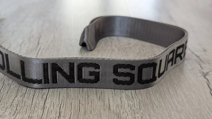 Close-up of a gray lanyard with the text 'ROLLING SQUARE' printed on it, placed on a wooden surface.
