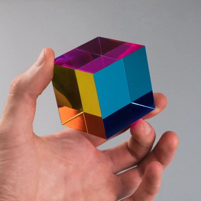 A person holding a colorful sensory cube made from acrylic, showcasing primary colors that blend into a spectrum when turned.
