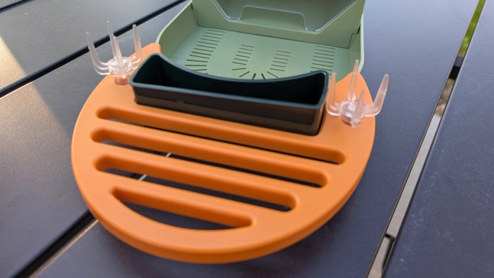 Close-up of the Vinguys Smart Bird Feeder's orange and green feeding tray, featuring a central black seed compartment and transparent perch supports.