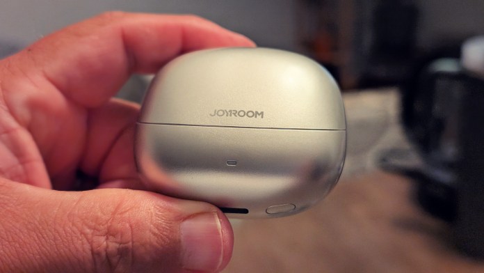 Close-up of a person holding the JOYROOM JR-OE3 open-ear earbuds charging case, featuring a sleek silver design with the JOYROOM logo.