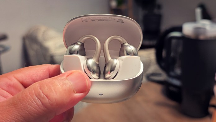 A person holding Joyroom JR-OE3 open-ear earbuds in a charging case with a blurry background, showcasing the sleek design and innovative features.
