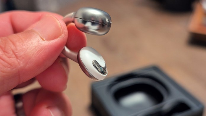 A close-up image of Joyroom JR-OE3 clip-on earbuds held in a person's hand, showcasing their sleek design and material details.