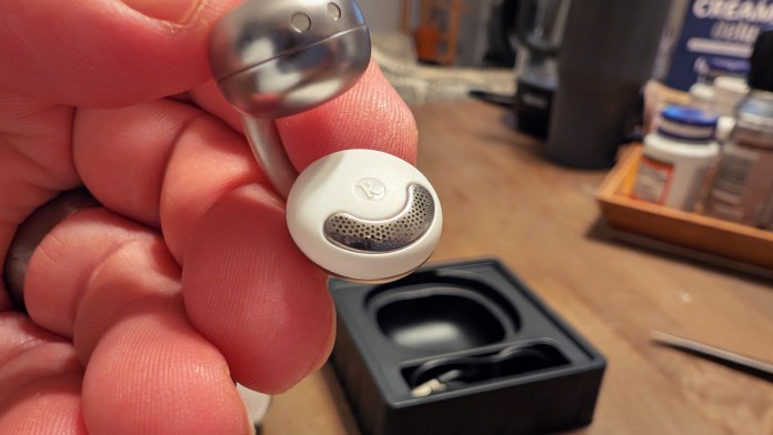 Close-up of Joyroom JR-OE3 Clip-On Earbud held by a hand, showcasing its sleek design and distinctive mesh speaker grill.