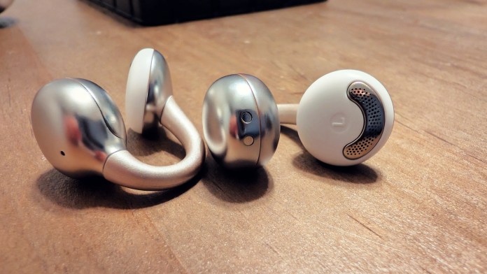 Close-up of Joyroom JR-OE3 open-ear earbuds, showcasing their sleek design and metallic finish on a wooden surface.