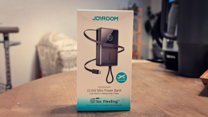 Joyroom JR-PR1 Retractable Power Bank packaging showcasing features such as 10000mAh capacity, 22.5W fast charging, and built-in retractable cable. The product is displayed on a table with a blurred background.