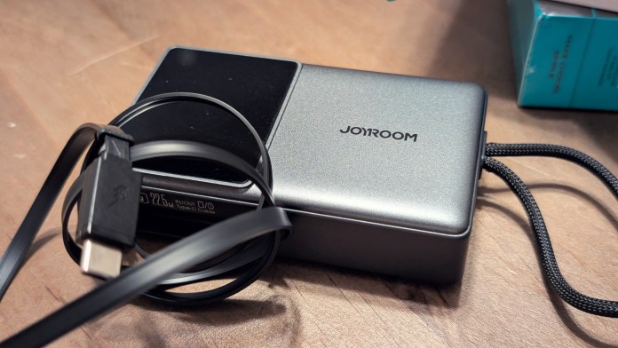 Joyroom JR-PR1 Retractable Power Bank on a wooden surface with a retractable Type-C cable attached, showcasing its compact design and digital display.