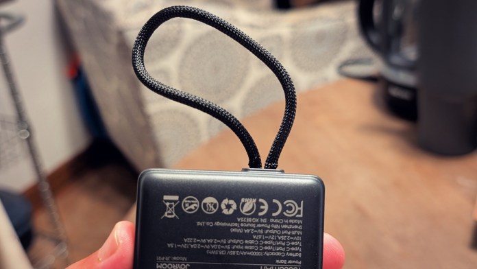 Close-up view of a hand holding a Joyroom JR-PR1 Retractable Power Bank, showcasing the retractable Type-C cable and the product specifications on the back.