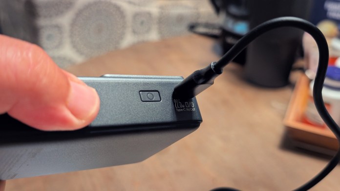 Close-up of a hand pressing the power button on a Joyroom JR-PR1 Retractable Power Bank with a Type-C cable connected, showcasing its compact design.