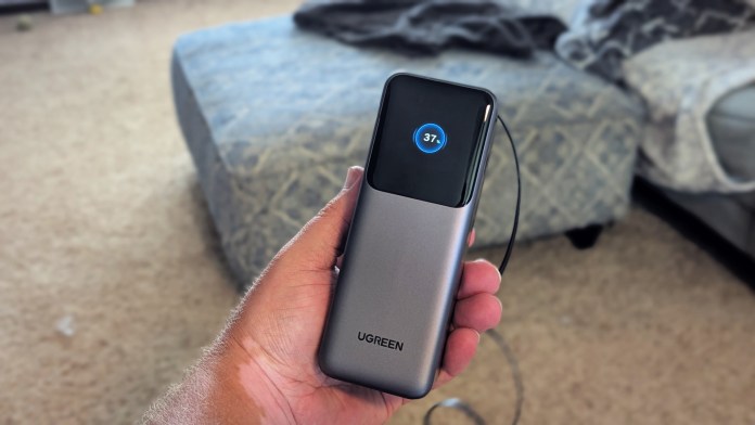 A person holding the UGREEN Retractable Series Power Bank, displaying a digital percentage indicator showing 37% charge, with a couch in the background.