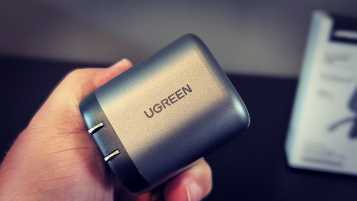 A person holding a UGREEN Nexode Retractable 145W Car Charger, showcasing its sleek design and branding.