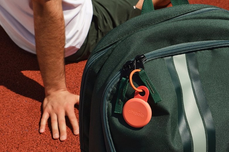 A Chipolo Loop item tracker attached to a green backpack on a red surface.
