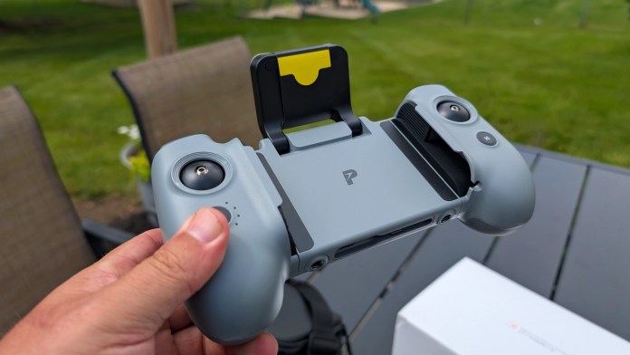 Close-up of the Potensic AT2-RC remote controller, showcasing its ergonomic design and phone holder, held in hand with a green lawn in the background.