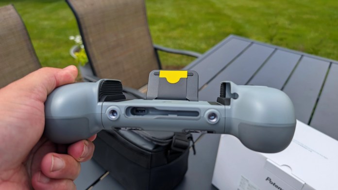 Close-up view of a hand holding the Potensic AT2-RC drone remote controller, showcasing its design and features, with a green outdoor background.