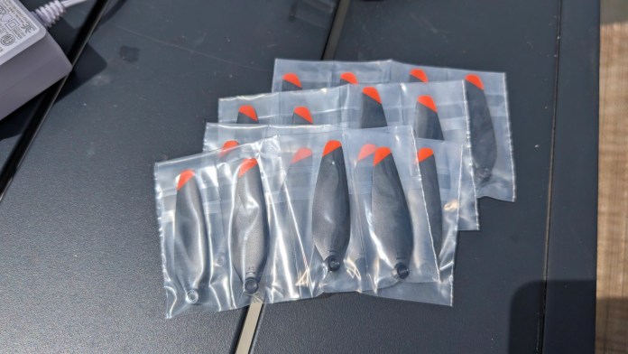 A collection of drone propellers in sealed plastic bags, featuring a red tip design, displayed on a flat surface.