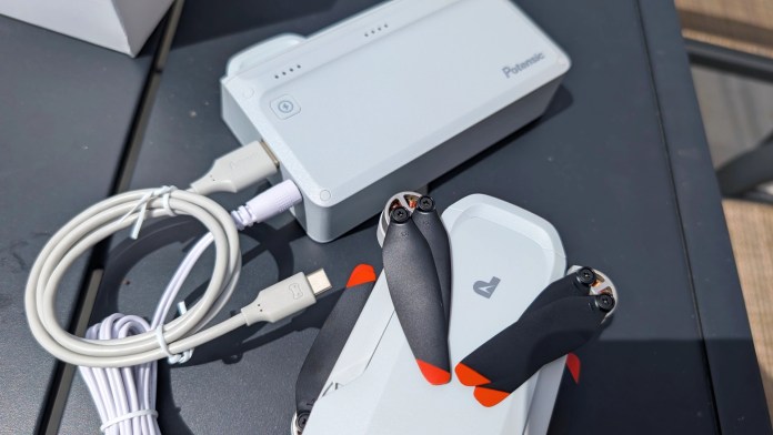 A Potensic drone battery, charging hub, and USB cables arranged on a table, showcasing the drone's compact accessories.