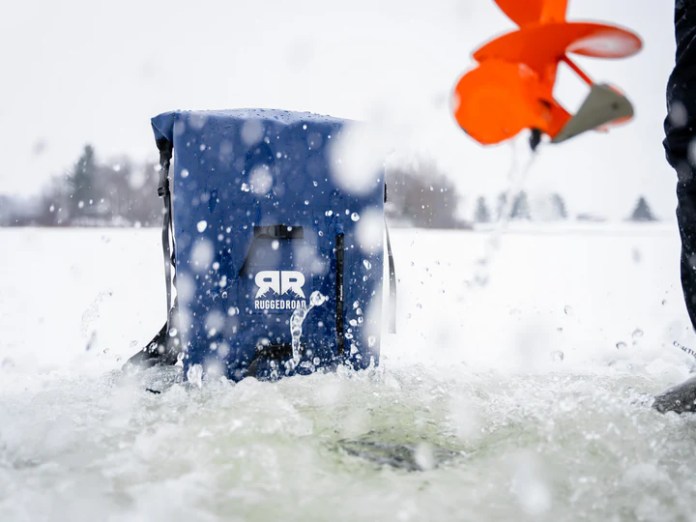 A Rugged Road cooler sitting in a snowy landscape, partially submerged in water, with splashes around it, showcasing its waterproof design.