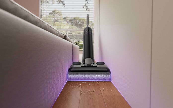 Eureka FloorShine 880 vacuum in action, cleaning between furniture with visible debris on the floor.