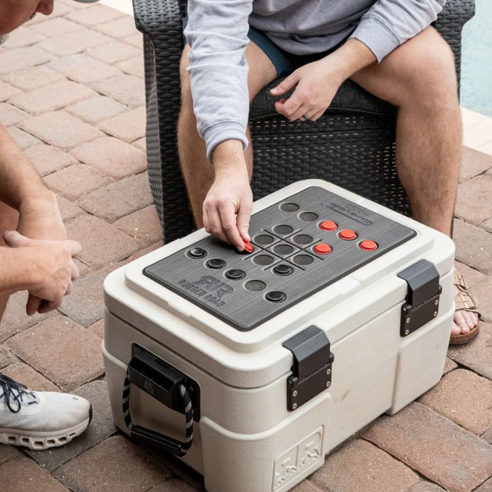 Two people playing a game on the lid of a Rugged Road cooler, featuring a textured surface and game pieces.