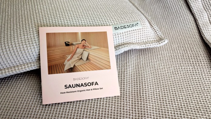 BADESOFA SAUNASOFA Mat & Pillow Set packaging on a textured fabric background, showcasing the luxury sauna accessory with an image of a woman relaxing in a sauna.