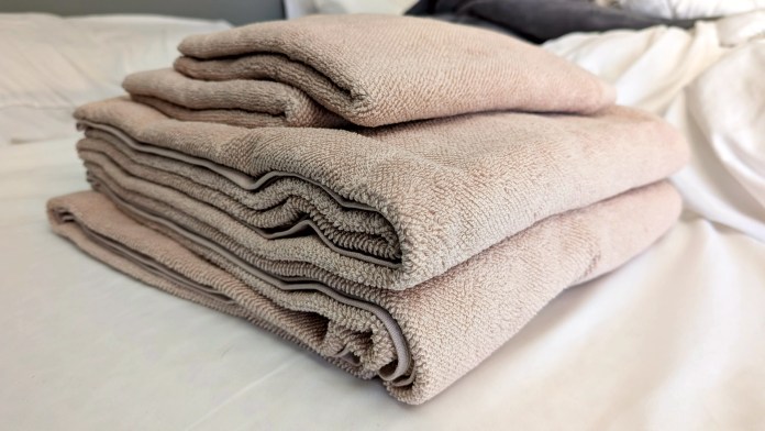 A neatly folded stack of BADESOFA Luxury Terry Towels in a soft beige color, displayed on a white surface.