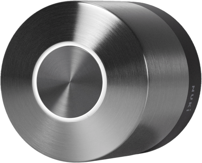 A close-up view of the Nuki Smart Lock, showcasing its sleek stainless steel design with a circular shape and a central button. The product features a brushed metal finish and a subtle glowing ring around the button.