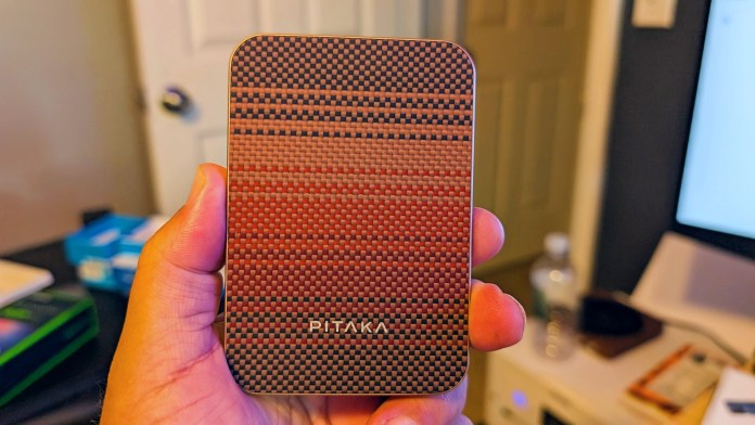 A person holding the PITAKA Aramid Fiber Magnetic Power Bank, showcasing its sleek design and textured surface featuring woven patterns.