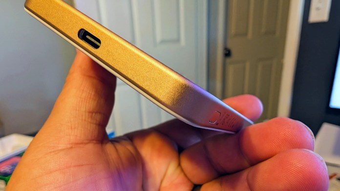 Close-up view of a hand holding a gold PITAKA Aramid Fiber Magnetic Power Bank, focusing on the USB-C port.