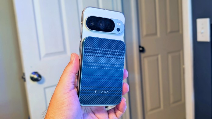 A hand holding a smartphone with a PITAKA Aramid Fiber Magnetic Power Bank attached to the back, showcasing the power bank's sleek design and magnetic connection.