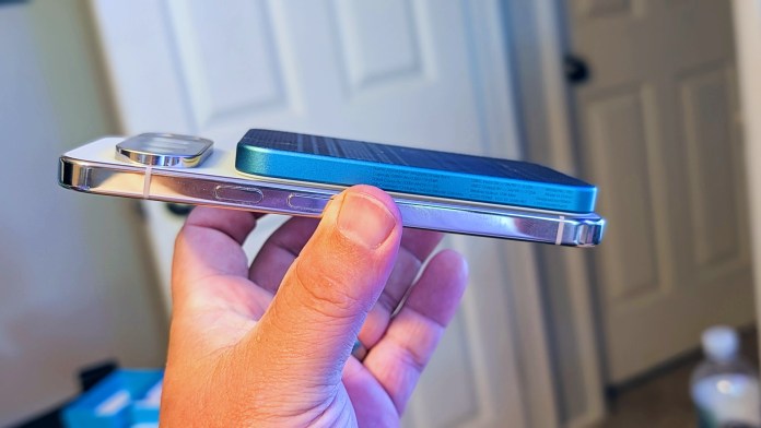 A hand holding a smartphone with a PITAKA Aramid Fiber Magnetic Power Bank attached to its back, showcasing the slim design and magnetic connection.