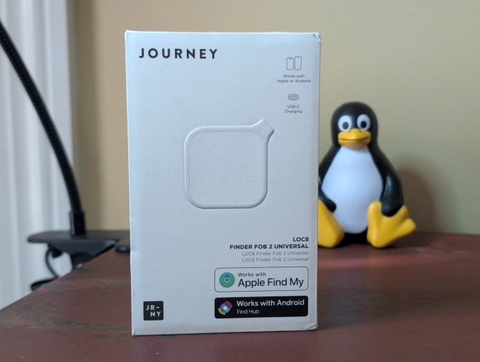 A box of the LOC8 Finder Fob 2 Universal by Journey, featuring compatibility with Apple and Android systems, with USB-C charging indicated. In the background, a small penguin figure is visible.