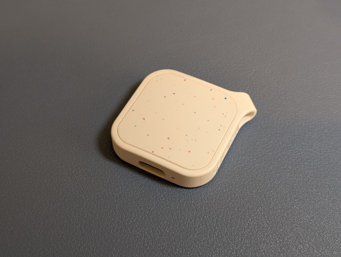 A small beige tracking fob with colorful speckles on a textured surface, showcasing its compact design and USB-C port.