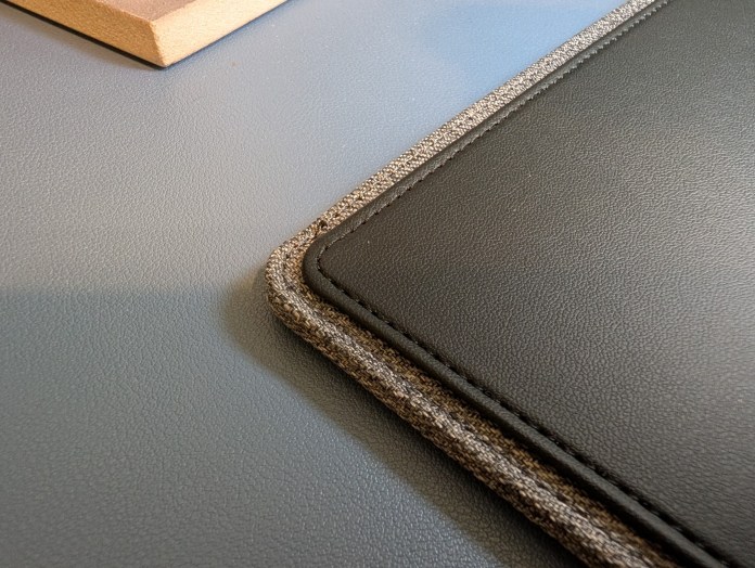 Close-up view of the stitching and edges of a black leather laptop sleeve with gray fabric detailing, placed on a smooth surface.