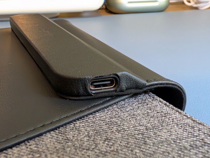 Close-up of the corner of the LOC8 Laptop Sleeve Universal showing the USB-C charging port on a black leather surface with a gray fabric background.