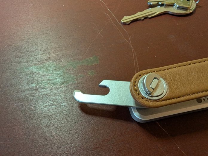 Close-up of the key holder's metallic clip mechanism with a leather strap and additional keys placed on a wooden surface.