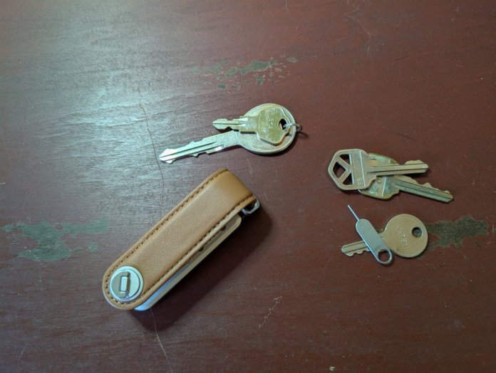 A LOC8 Urban Key Organizer in brown leather displaying several keys arranged beside it, set against a wooden surface.