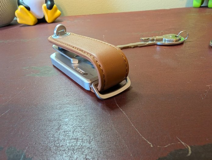 A brown leather key organizer resting on a red surface, with keys attached, showcasing a sleek and compact design.