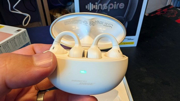 A person's hand holding a white charging case with two wireless earbuds inside, with a visible green indicator light.