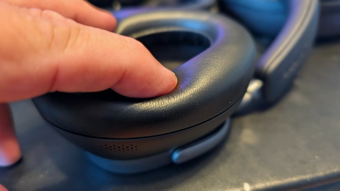 Close-up of a person's hand pressing on the padded ear cup of an over-ear headphone, showcasing its soft material and design.