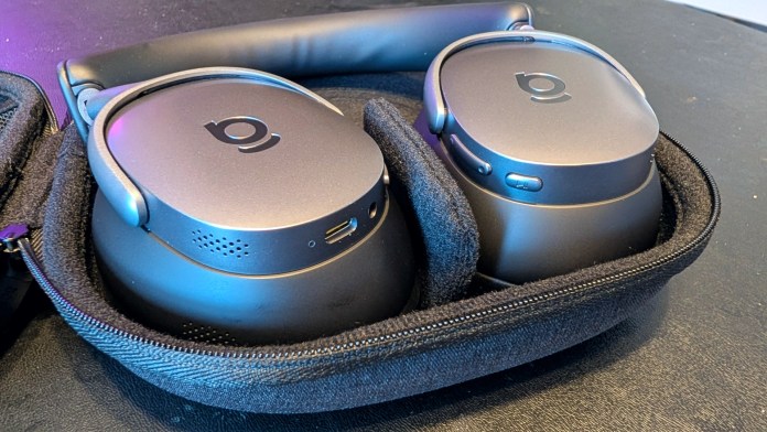 Close-up view of Baseus Inspire XH1 noise-cancelling headphones, displayed inside a protective case, showcasing their sleek design and charging port.