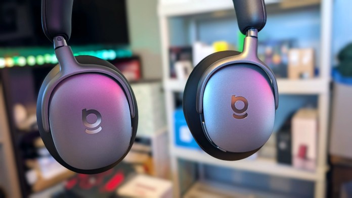 Close-up view of the Baseus Inspire XH1 Noise-Cancelling Headphones displaying their sleek design and branding against a blurred background of various tech products.
