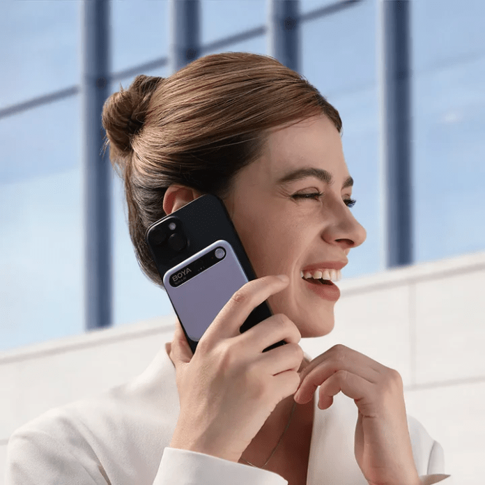 A woman smiling while holding a smartphone to her ear, dressed in a white outfit, with a modern building in the background.